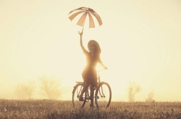 Girl-with-umbrella-on-a-bike-in-the-countryside-in-sunrise-time