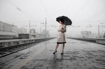 Woman-with-umbrella-standing-on-the-platform-of-a-train-station